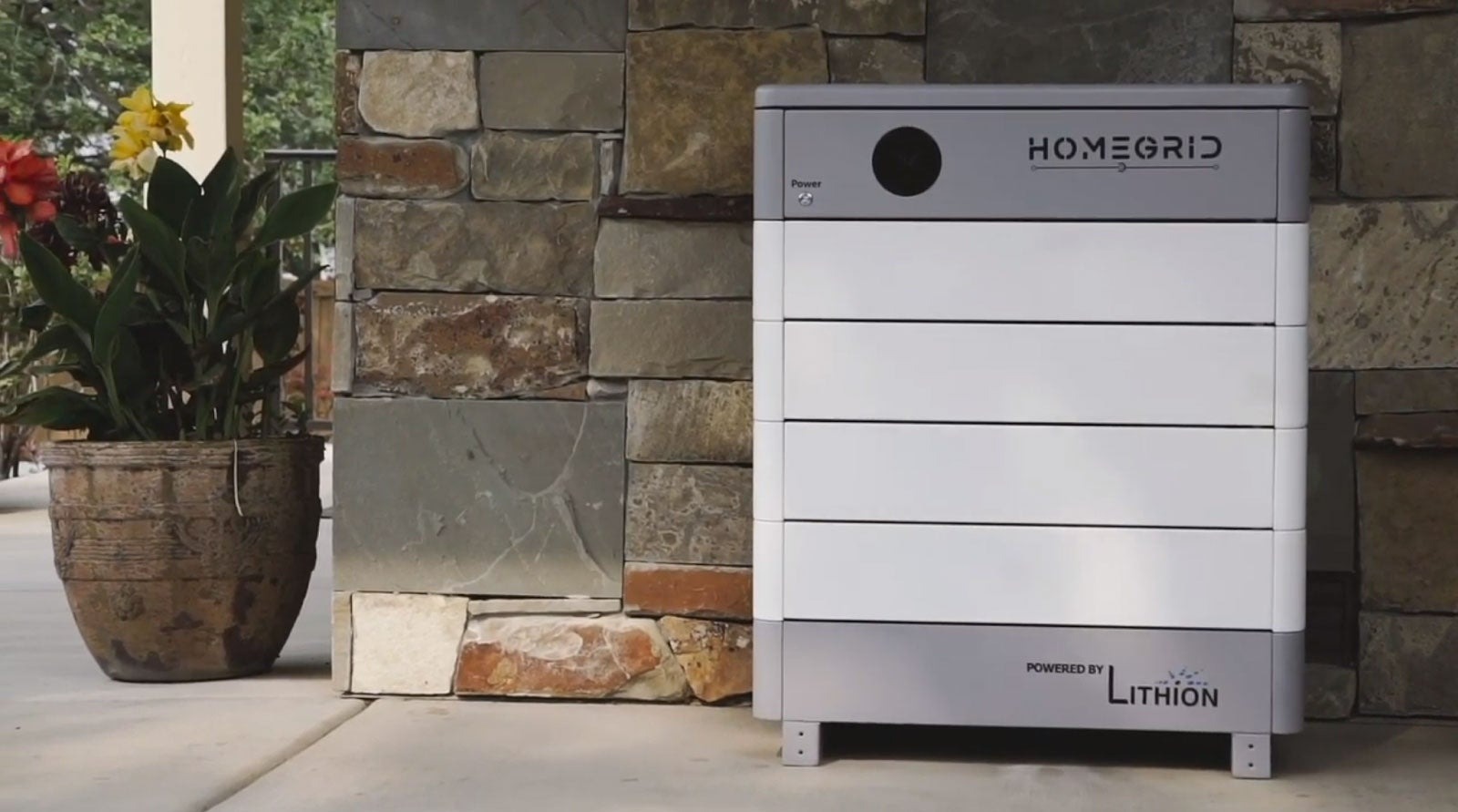 A photo of a HomeGrid Stack'd series battery in front of the exterior wall of a home